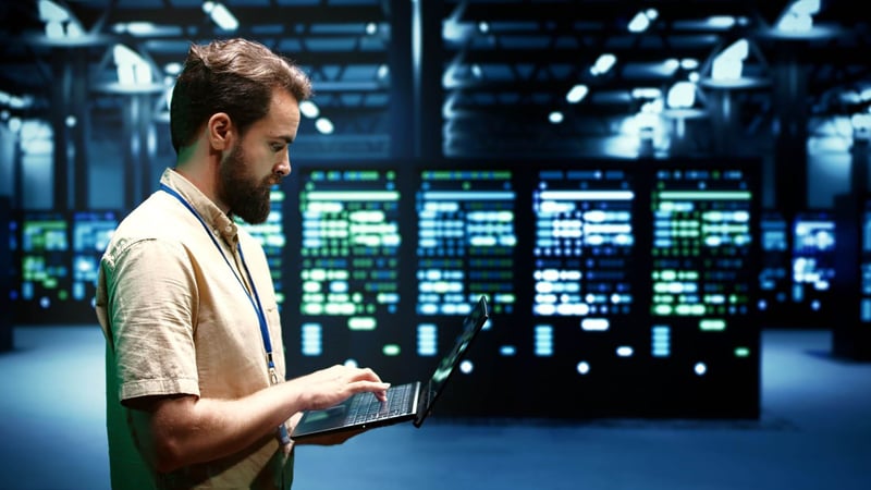 engineer on laptop walking through data center